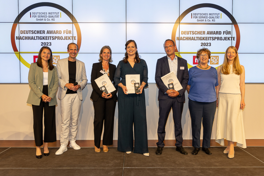 Die Gewinnerinnen und Gewinner in der Kategorie Aufklärung/Bildung stehen vor einer Wand, auf der das Logo des Deutschen Awards für Nachhaltigkeitsprojekte 2023 zu sehen ist. Drei von ihnen halten Urkunden in der Hand.
