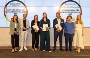 Die Gewinnerinnen und Gewinner in der Kategorie Aufklärung/Bildung stehen vor einer Wand, auf der das Logo des Deutschen Awards für Nachhaltigkeitsprojekte 2023 zu sehen ist. Drei von ihnen halten Urkunden in der Hand.