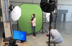 Eine Frau steht vor einem Greenscreen während ein Mann Fotos von ihr macht.