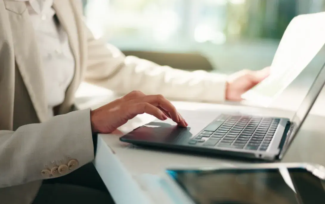 Eine Person bedient einen Laptop und hält in der anderen Hand ein Blatt Papier.