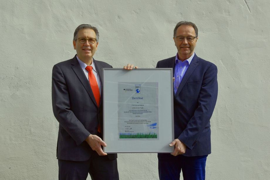 Das Bild zeigt Aschaffenburgs Oberbürgermeister Jürgen Herzing und Walter Hartmann, Leiter des Amts für Hochbau und Gebäudewirtschaft in Aschaffenburg, mit dem Klimaschutz-Zertifikat in den Händen.