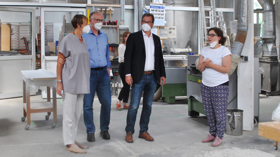 Das Bild zeigt die Baufachfrau-Geschäftsführerin Heike Eskandarinezhad, den Bundestagsabgeordneten Klaus Mindrup, den Parlamentarischen Staatssekretär Florian Pronold und Tischlermeisterin Franziska Müller, wie sie nebeneinander in der vereinseigenen Tisc