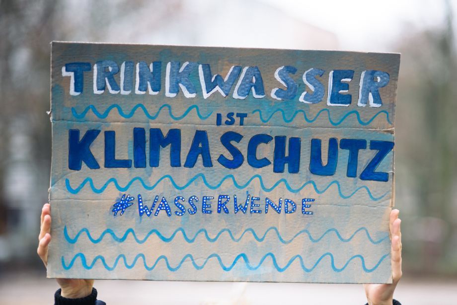 Das Bild zeigt ein gemaltes Plakat mit der Aufschrift „Trinkwasser ist Kilmaschutz. Hashtag Wasserwende.