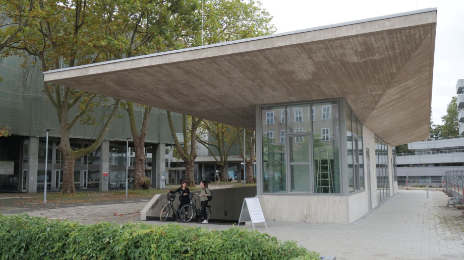 Das Bild zeigt die neue Fahrradstation an der Universität zu Köln und eine Studierende und Mitarbeitende mit ihren Fahrrädern in der Einfahrt des Gebäudes.