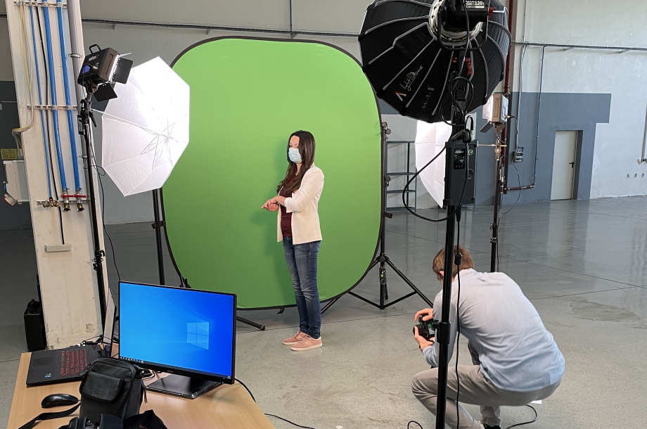 Eine Frau steht vor einem Greenscreen während ein Mann Fotos von ihr macht.