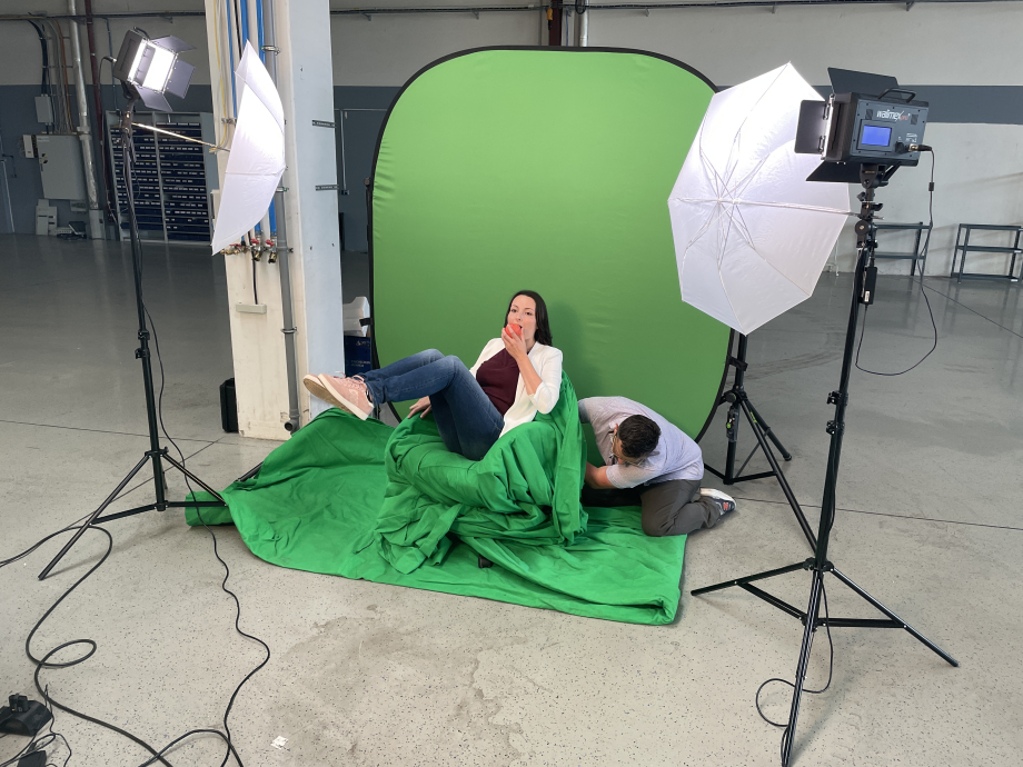 Eine Frau in einem grünen Stuhl vor einem Greenscreen und isst einen Apfel.