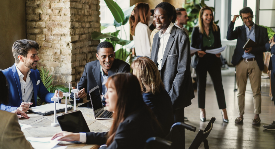 Menschen im Business-Outfit tauschen sich bei einem Vernetzungstreffen an einem großen Tisch und im Raum aus.