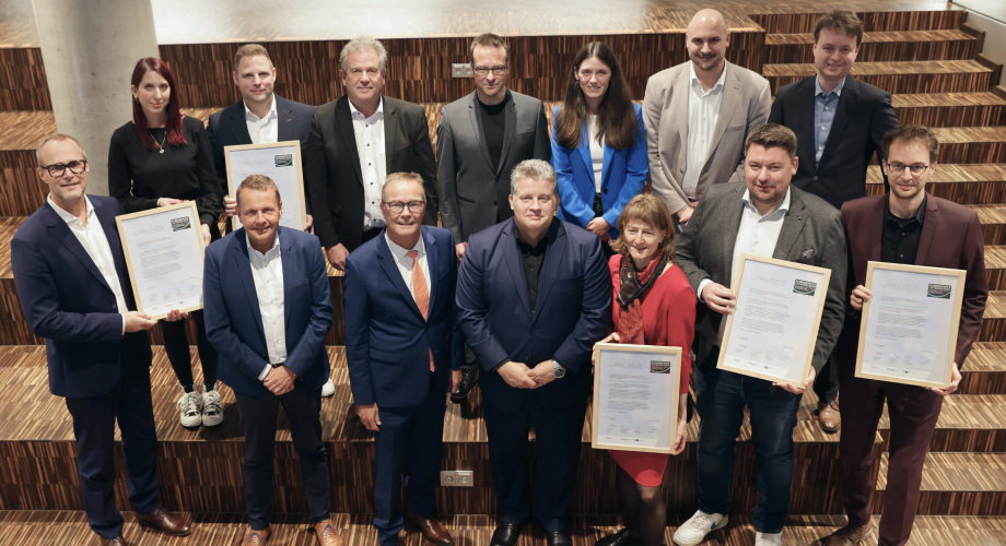 Eine Gruppe von Menschen steht auf einer Treppe und hält Urkunden für ihr klimafreundliches Unternehmensengagement.