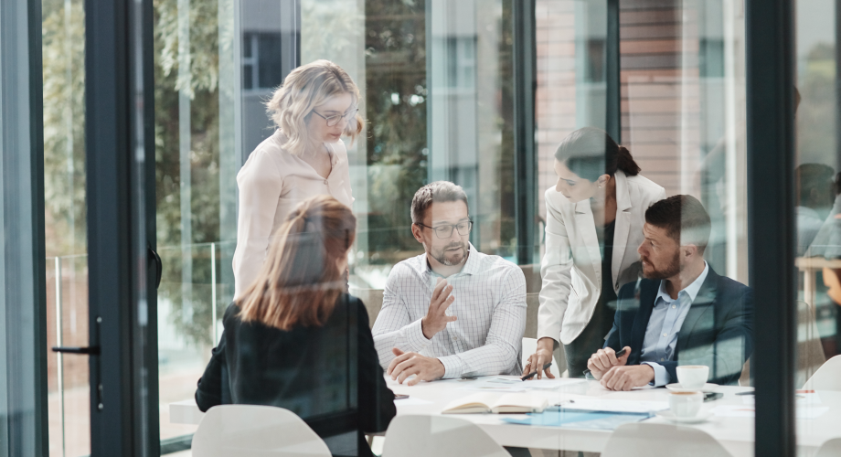 Mehrere Personen besprechen sich an einem Konferenztisch in einem hellen Büro mit großen Glasflächen.