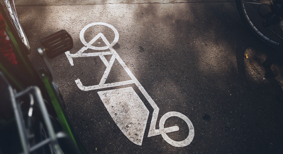 Fahrradsymbol ist auf Asphalt markiert, eingerahmt von abgestellten Fahrrädern.