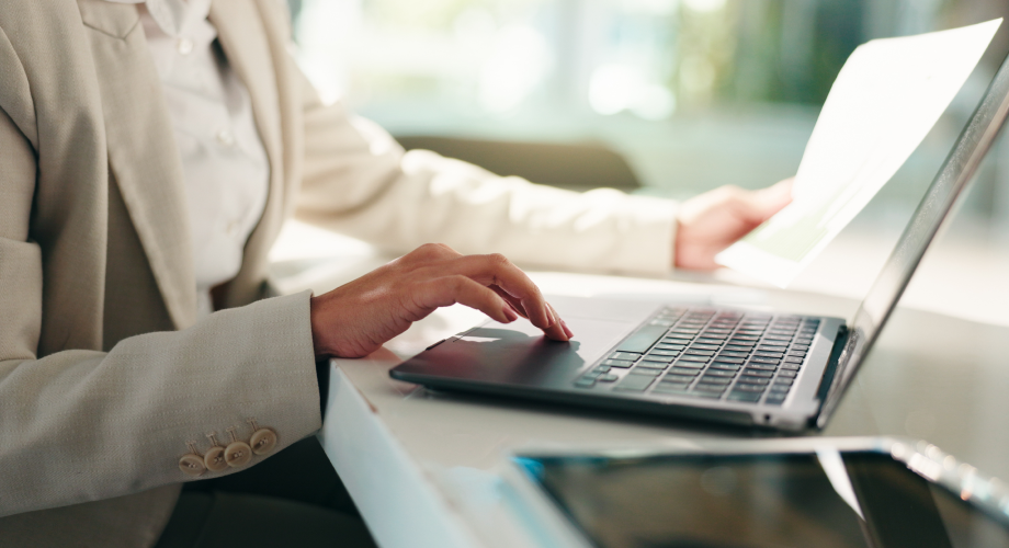 Eine Person bedient einen Laptop und hält in der anderen Hand ein Blatt Papier.