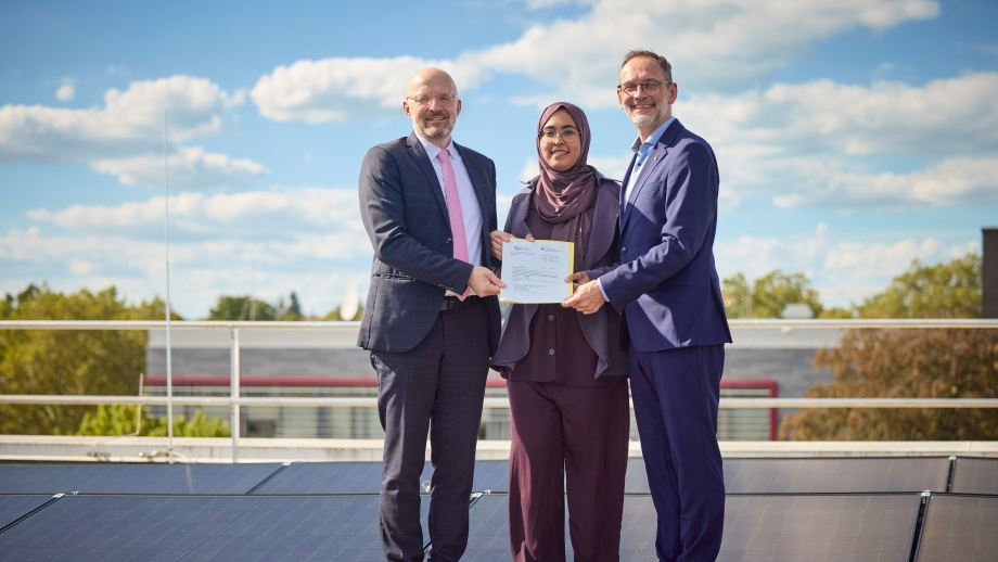 Drei Personen stehen vor Solarmodulen der Universität Bonn und halten gemeinsam den Förderbescheid in die Kamera.
