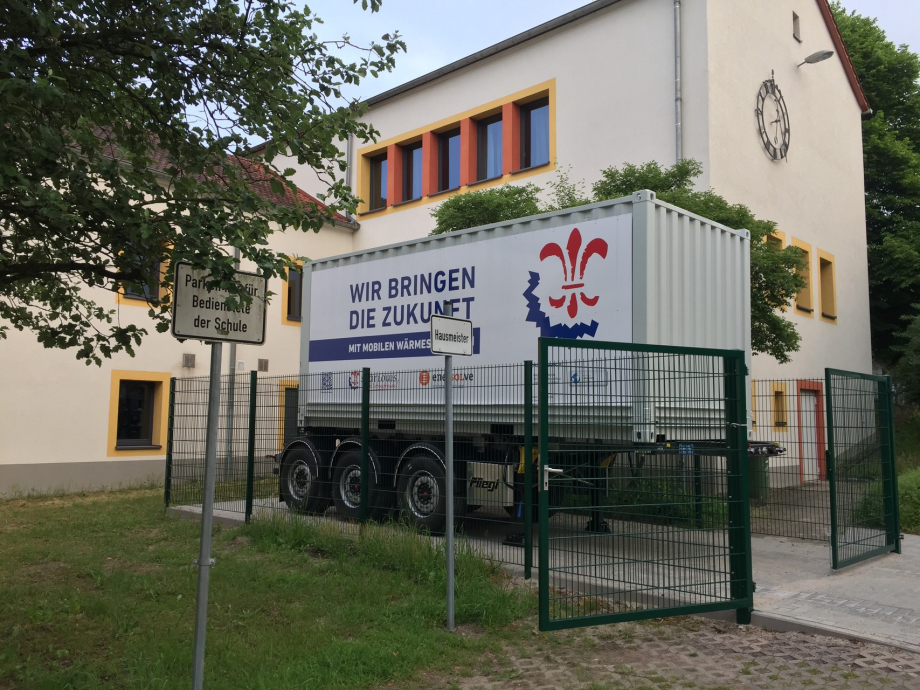 Ein LKW-Anhänger steht vor einem Haus, drumherum ein Zaun