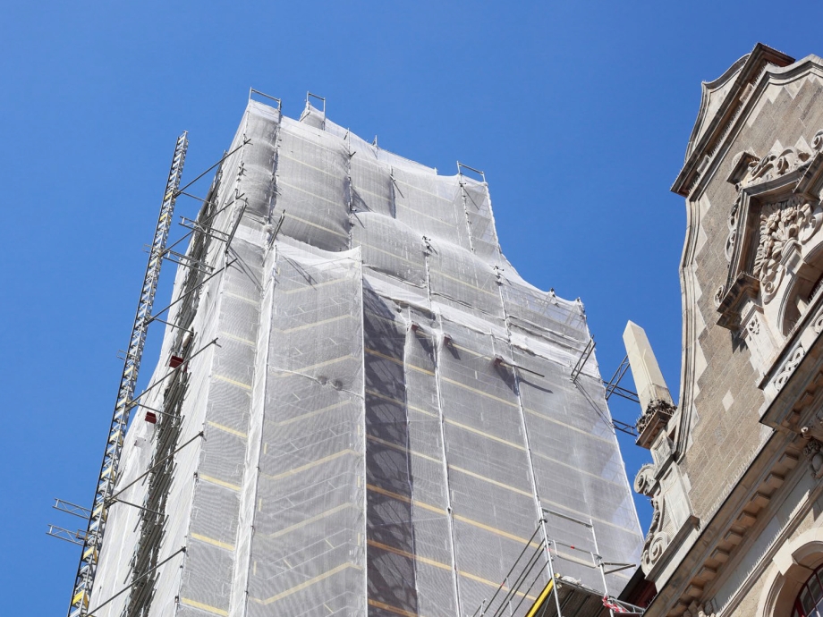 Von Gerüst und Schutznetz umhülltes hohes Gebäude vor blauem Himmel