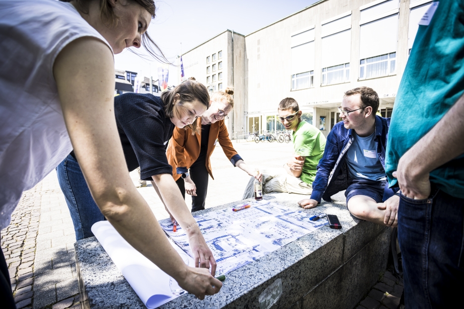 Junge Erwachsene diskutieren im Freien aktiv Pläne und Karten bei einer Projektrunde zur Verkehrswende.