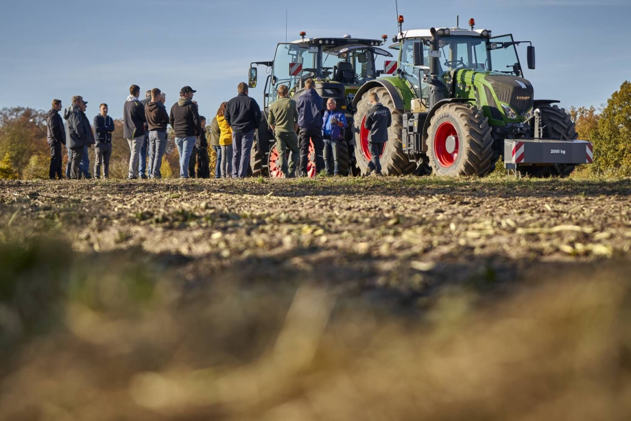 Foto von zwei Traktoren die auf einem Acker stehen. Davor steht eine Gruppe Menschen.