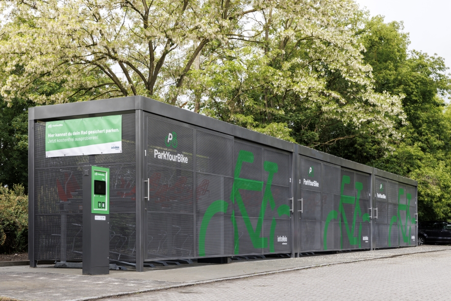 Große, moderne Fahrradabstellanlage „ParkYourBike“ mit gesichertem Zugang und Infotafel im Grünen.