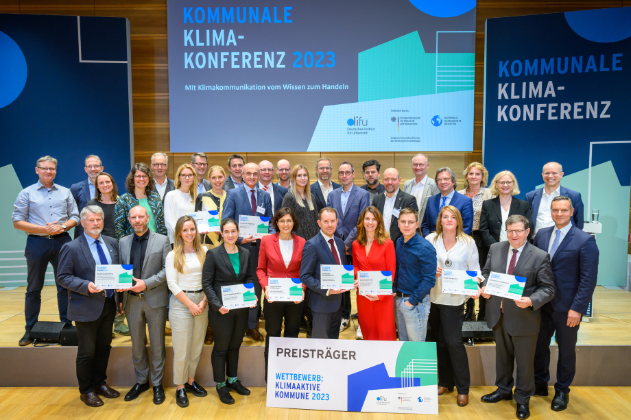 Die Teams der ausgezeichneten Kommunen des Wettbewerbs „Klimaaktive Kommune 2023“ stehen gemeinsam mit den Gratulierenden auf der Bühne