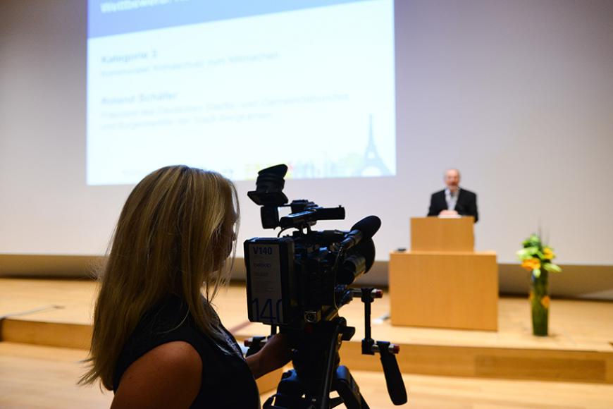 Kamerafrau mit Blick aufs Podium und einen Sprecher beim Wettbewerb Klimaaktive Kommune 2015