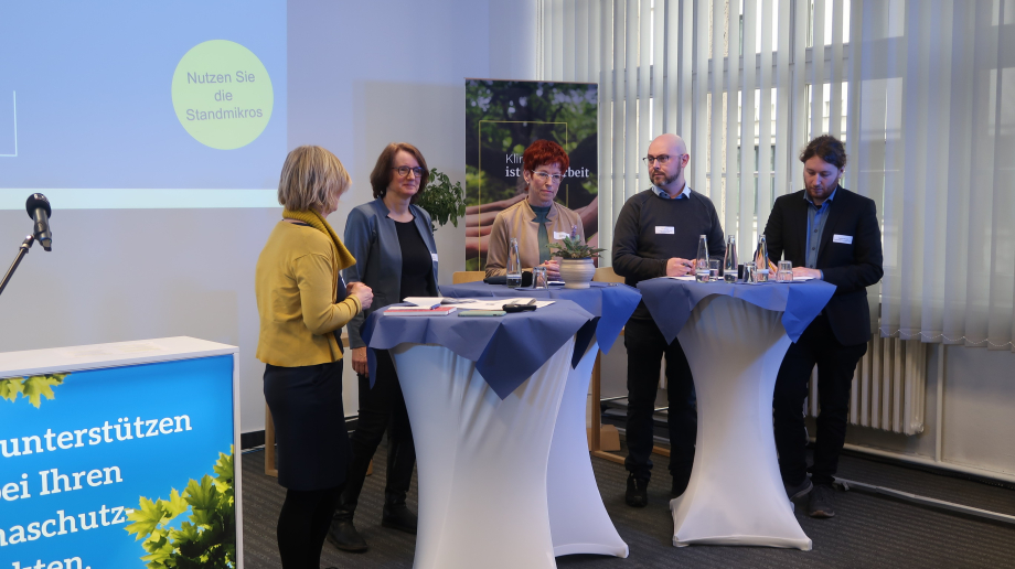 Das Foto zeigt das Podium der Veranstaltung "Bausteine der kommunalen Wärmewende" mit drei Stehtischen und fünf Personen, die sich im Austausch befinden.