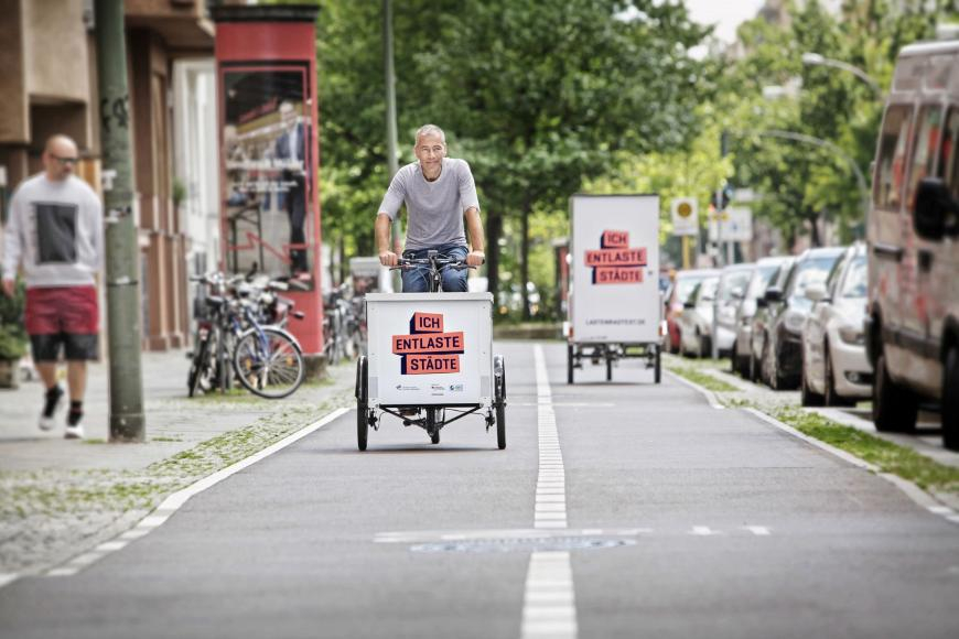 Das Bild zeigt zwei Lastenrad fahrende Personen auf einem breiten Fahrradweg. 