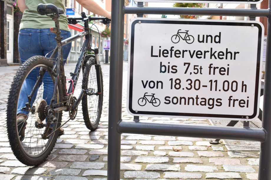 Das Bild zeigt ein Straßenschild und eine Radfahrerin.