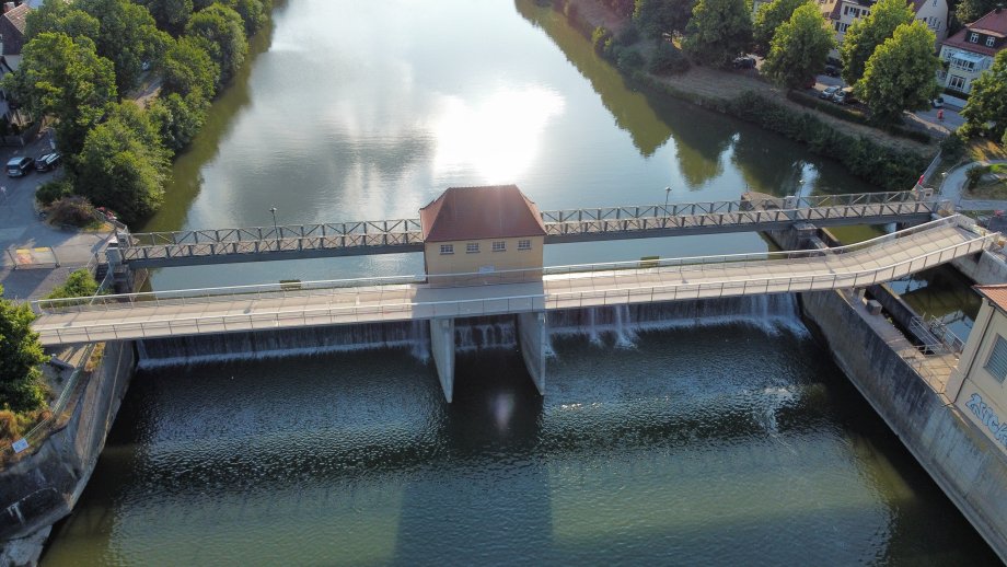 Vogelperspektive einer Brücke von oben. Links und rechts vom Fluss wachsen Bäume.