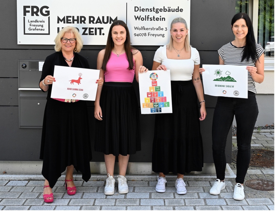 Vier Personen stehen vor einem Dienstgebäude des Landkreises Freyung-Grafenau und halten Schilder mit Abbildungen in den Händen.