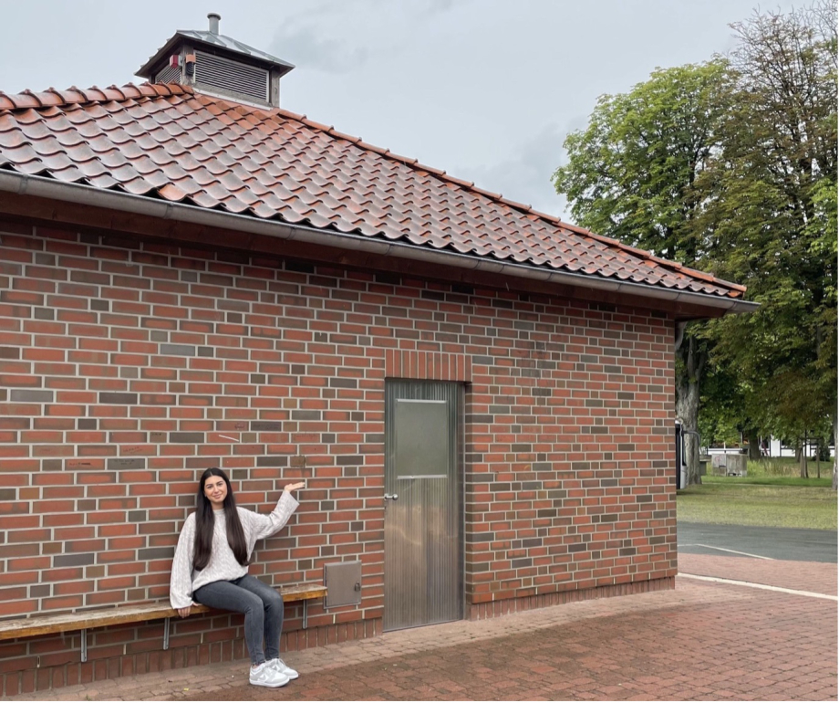 Eine Jugendliche sitz auf einer Bank vor einem Backsteinhaus.