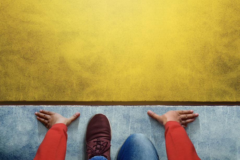 Der Hintergrund ist zweifarbig. Das untere Drittel ist blau und wird durch eine braune Linie von der gelben Farbe getrennt. Vor der Linie sind die Hände und Füße einer Person in der Startposition für einen Sprint zu sehen. 