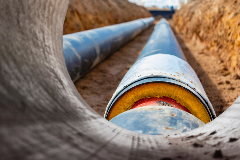 Auf dem Bild zu sehen sind zwei Rohre aus der Froschperspektive. Große Metallrohre mit einer Kunststoffhülle, die in einem Graben gelegt ist. Moderne Pipeline zur Versorgung eines Wohngebiets mit Warmwasser und Heizung.