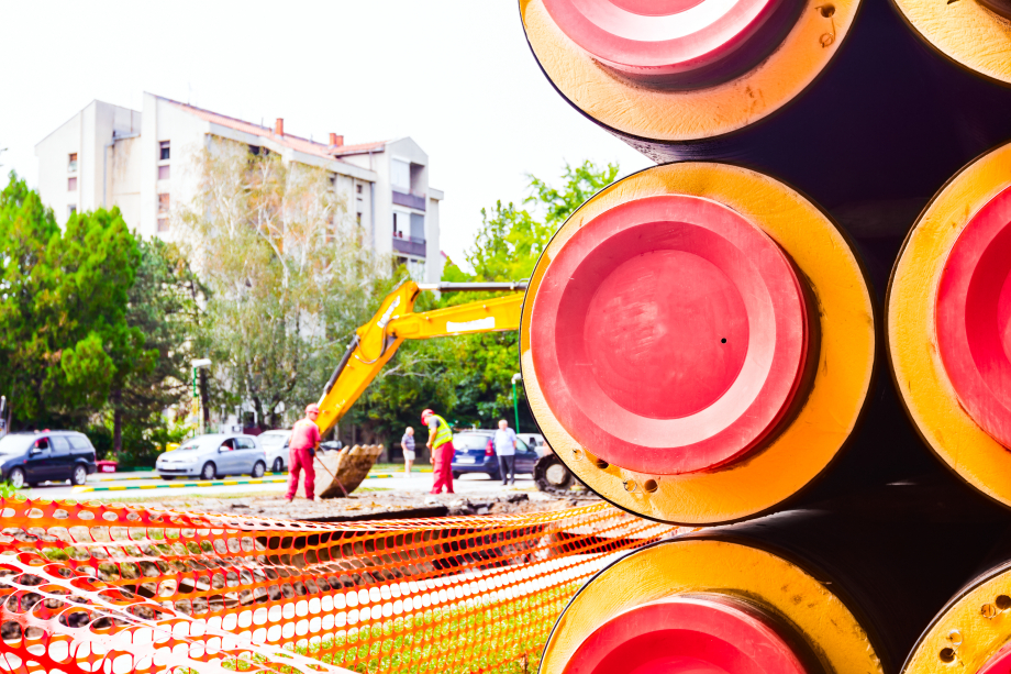 Das Foto zeigt eine Seitenansicht auf rot-orange Rohre, sowie eine Baustelle im Hintergrund