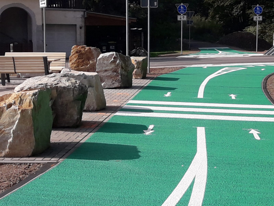 Foto von einem neuen Radweg. Der im Bild zu sehende Abschnitt ist grün und die Fahrtrichtung ist mit Pfeilen gekennzeichnet. Am Wegrand stehen große Steine.