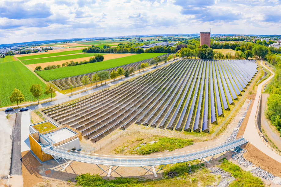 Ein Steg führt auf ein Technikgebäude, von dem aus man über ein Solarfeld blickt