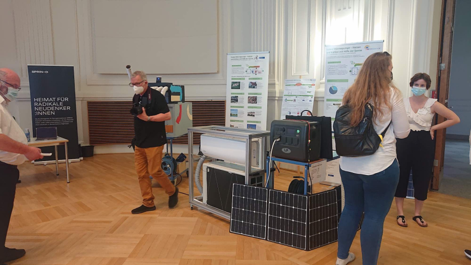 Der Stand des Projekts „Solare Wärmepumpe – Heizen und Kühlen mit Hilfe der Sonne“ (DESWENDE), zu sehen sind Besucherinnen und Besucher vor dem Wärmepumpendemonstrator 