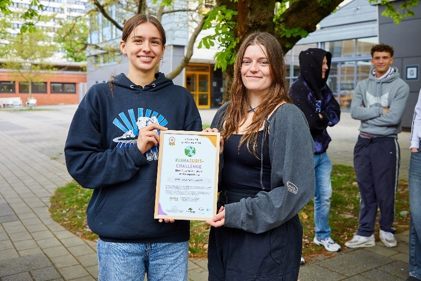 Zwei Jugendliche präsentieren im Freien eine Urkunde zur erfolgreichen Teilnahme an der Klimazubis-Challenge.