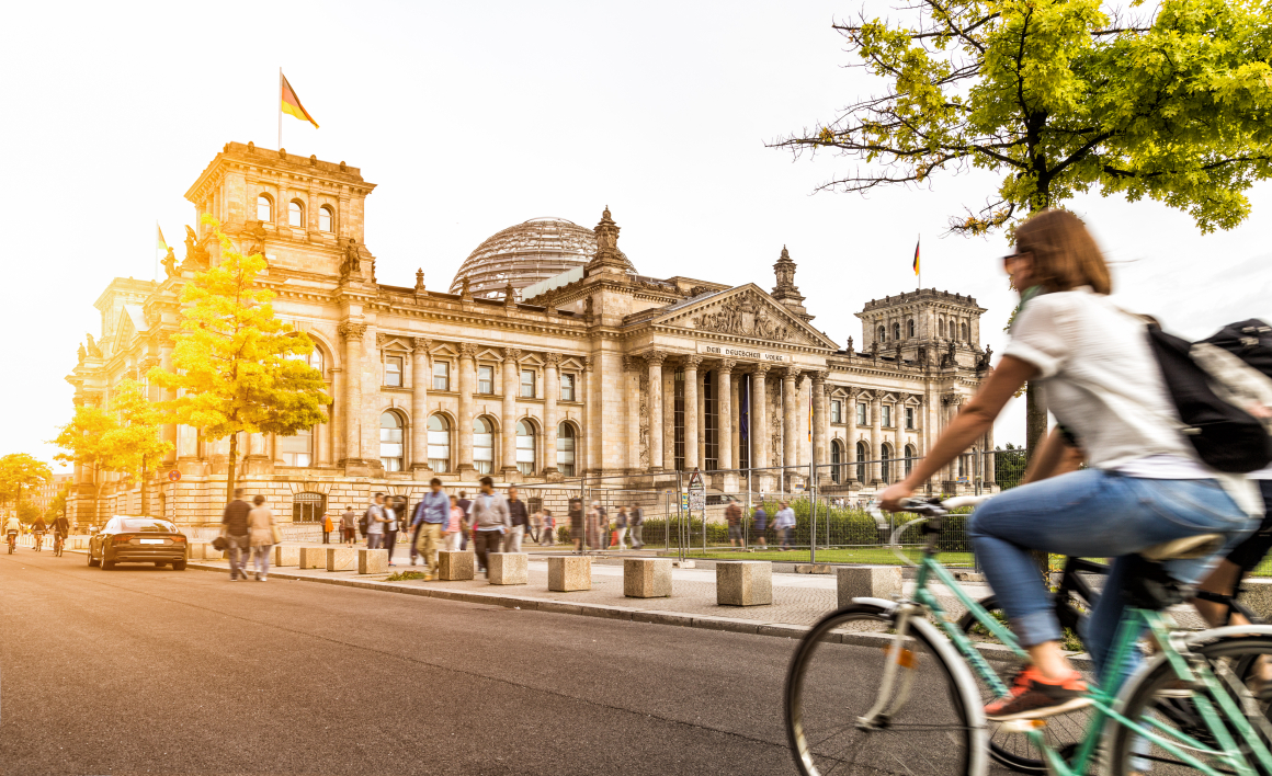 Der Bundestag in Berlin im Sonnenlicht, davor eine Radfahrerin