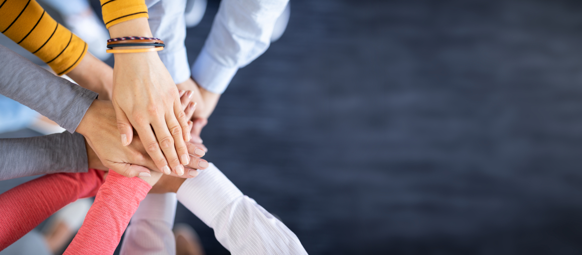 Fünf paar Hände aufeinander gelegt, um Teamwork zu symbolisieren