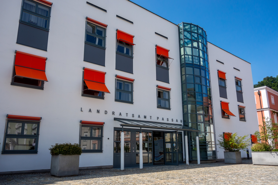 Außenansicht des Landratsamtes Passau, eines relativ modernen Verwaltungsgebäudes mit orangefarbenen Verschattungsvorrichtungen vor den Fenstern, vor blauem Himmel