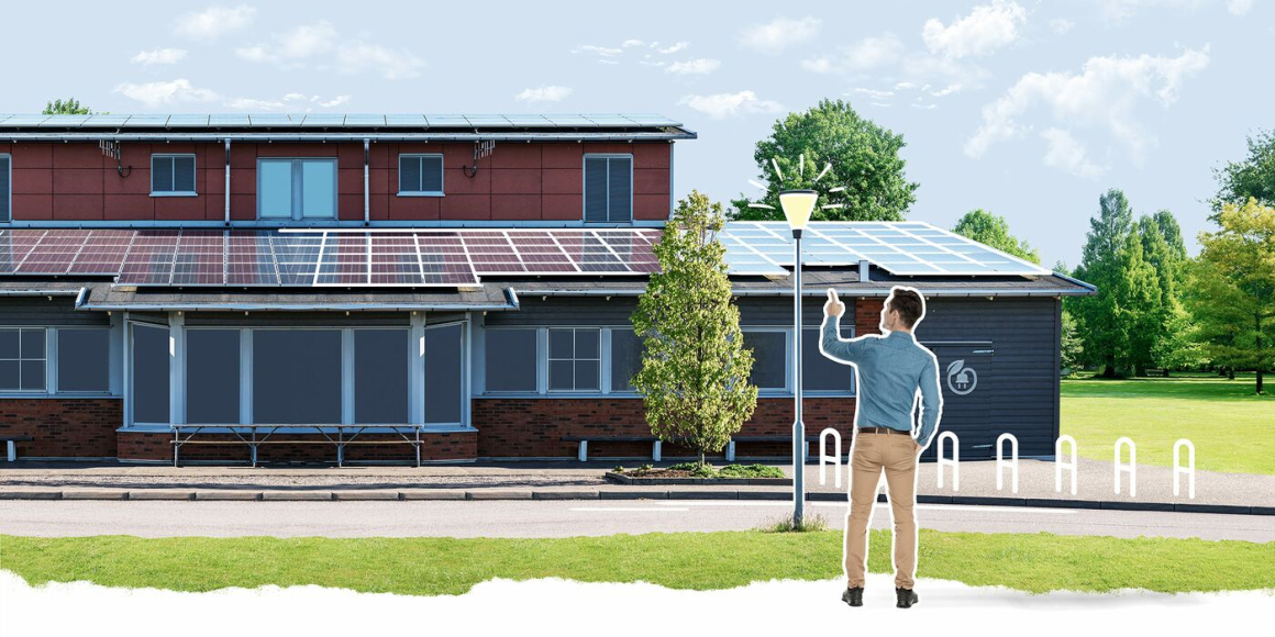 Ein Klimaschutzmanager vor einem kommunalen Gebäude, auf dessen Dach Photovoltaik-Module angebracht sind. Vor dem Gebäude steht eine Straßenlaterne, deren Beleuchtung auf LED umgerüstet wurde.