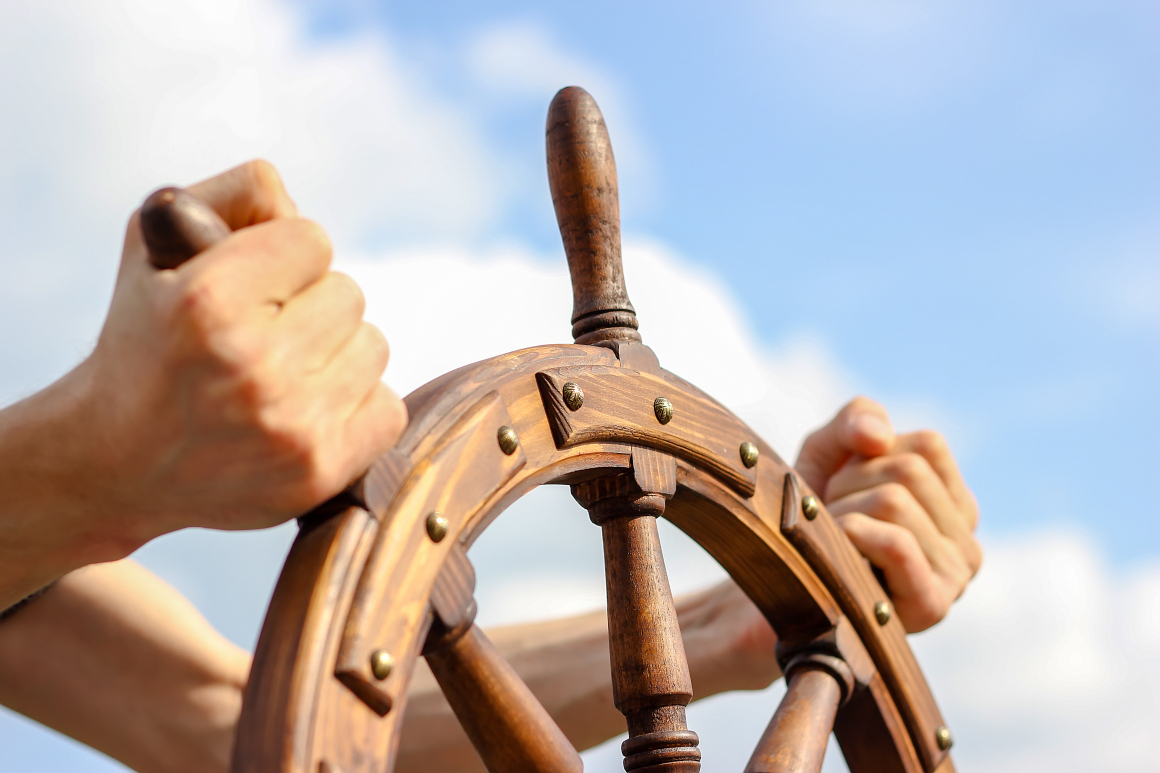 Eine Hand umklammert fest das Steuerrad eines Schiffes