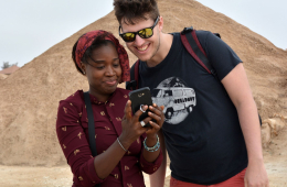 Das Bild zeigt ein Mädchen of Color und einen Jungen, die gemeinsam auf ein Smartphone blicken. 