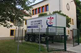 Ein LKW-Anhänger steht vor einem Haus, drumherum ein Zaun
