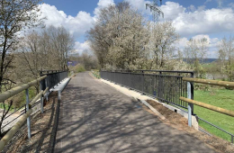 Foto von einem Radweg der über eine Brücke mit Stahl-Holz-Geländer führt