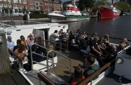 Die Teilnehmenden sitzen unter freiem Himmel auf dem Deck des Boots.