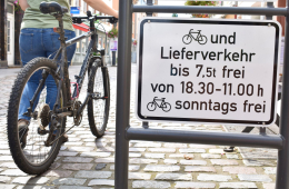 Das Bild zeigt ein Straßenschild und eine Radfahrerin.