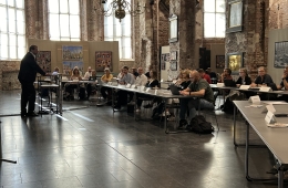 Der Oberbürgermeister steht an einem Redepult, vor ihm sitzen die Teilnehmenden an langen Tischen.