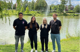 Vier Personen stehen vor einem Teich mit Springbrunnen im Grünen.