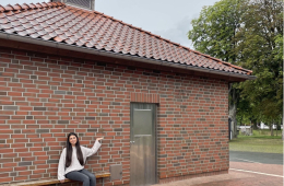 Eine Jugendliche sitz auf einer Bank vor einem Backsteinhaus.