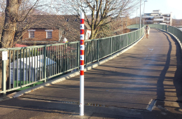 Eine Brücke mit Fahrradweg. Am Anfang des Radwegs ist mittig ein rot-weiß gestreifter Absperrpoller installiert.